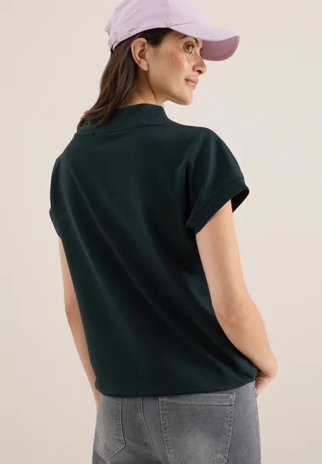 Frau mit lila Kappe, dunkelgrünem Shirt und Jeans von hinten.